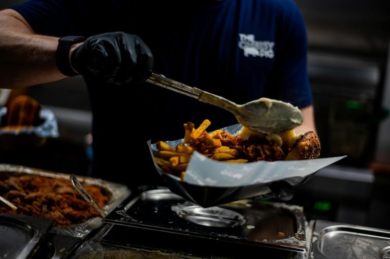 A chef in a street food stall prepares delicious loaded fries with cheese and meat.