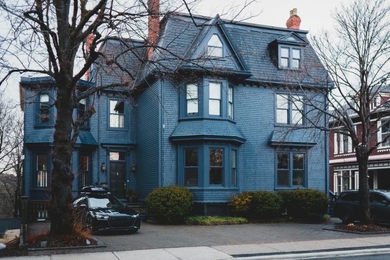 Exterior of blue contemporary residential house with bushes and trees and cars parked near pavement