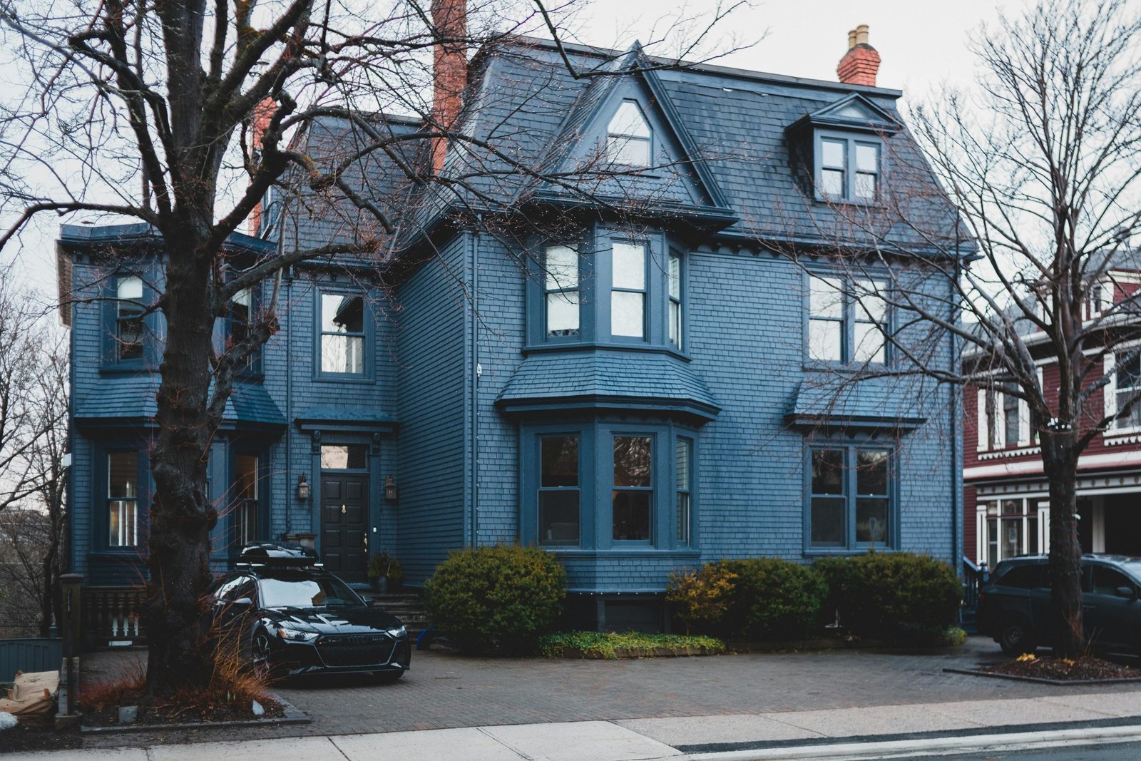 Exterior of blue contemporary residential house with bushes and trees and cars parked near pavement