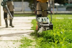 Two men operating a lawn mower as part of a lawn care service, cutting grass in a residential yard.