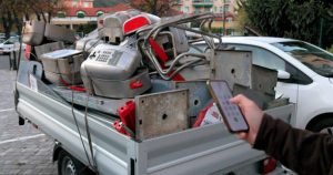 A man holds a remote control beside a truck filled with junk, promoting appliance removal and recycling services.
