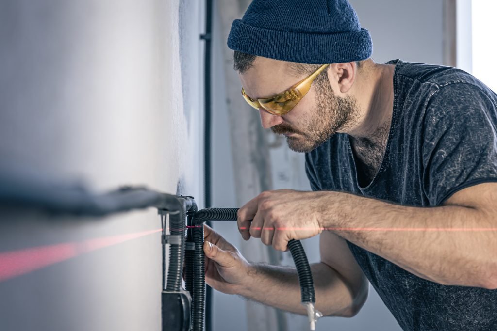 Attractive male electrician repairing an outlet, installing an outlet using laser marking.