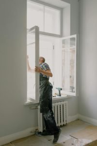 Side view of anonymous handyman in uniform mounting window frame during renovation process in flat