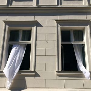 Elegant Berlin building facade with windows and flowing curtains in sunlight.