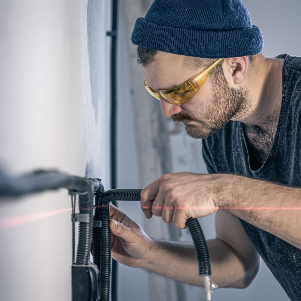 Attractive male electrician repairing an outlet, installing an outlet using laser marking.